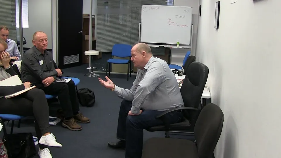 Rick Collingwood seated at the front of a training room, gesturing as he talks to students taking notes
