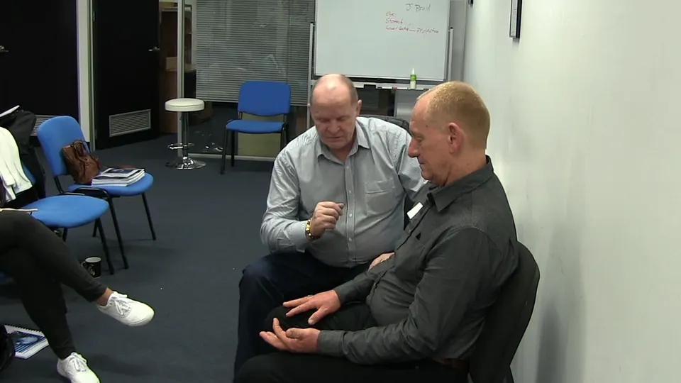 Rick Collingwood seated beside a male student, demonstrating with his hand while the student rests his hands in his lap
