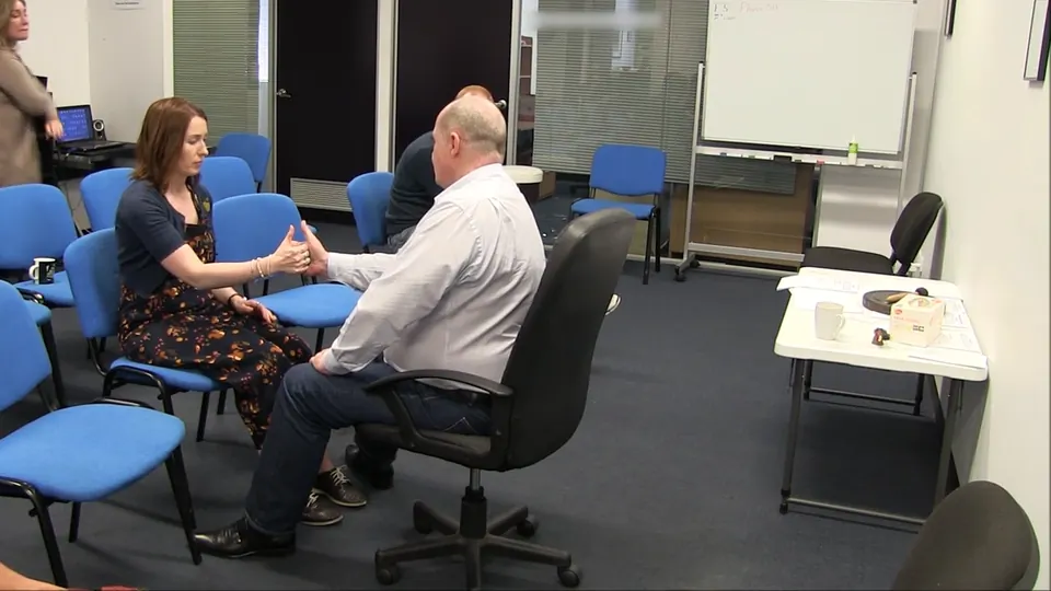 Rick Collingwood seated opposite a woman, holding her hands between his during a demonstration
