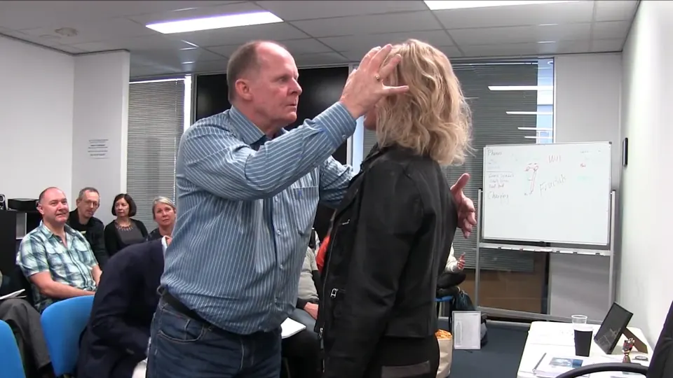 Rick Collingwood placing a hand on a standing student's head as the class watches