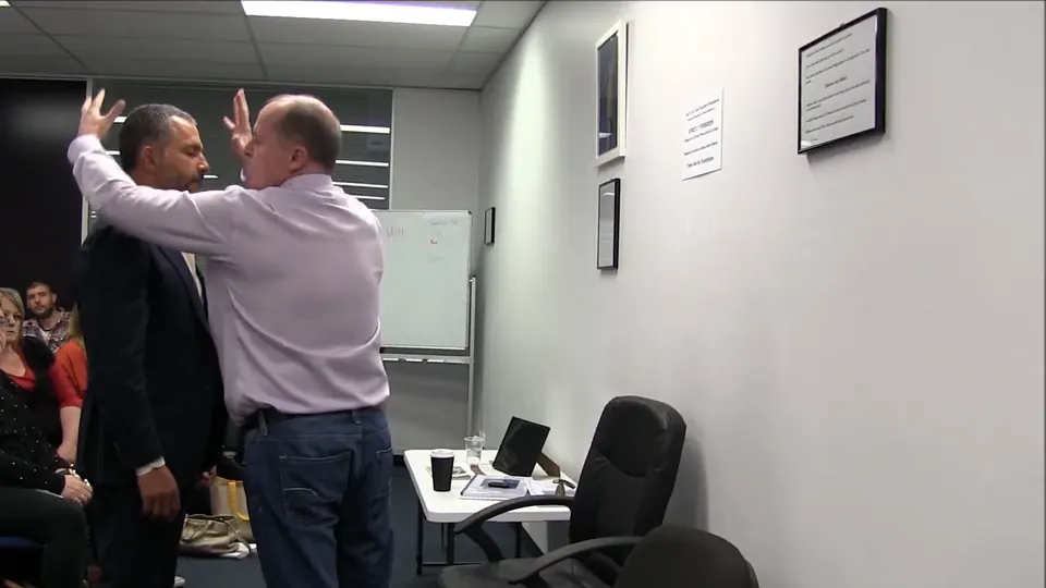 Rick Collingwood raising his hands beside a standing student in front of the class