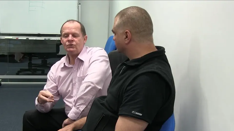 Rick Collingwood seated beside a student, explaining a point in a training session