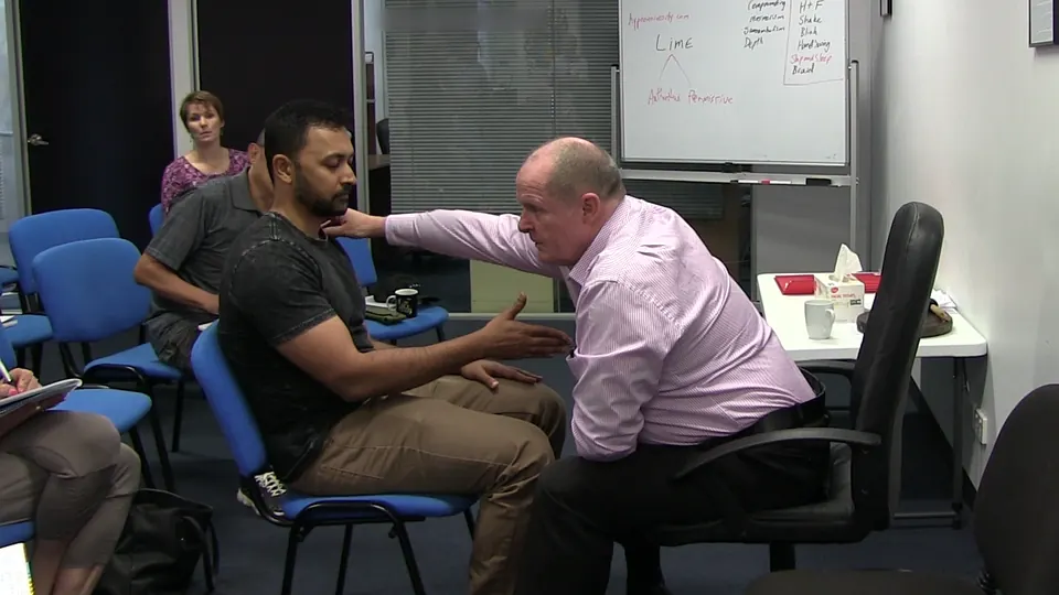 Rick Collingwood reaching towards a seated male student during a demonstration, with students seated behind