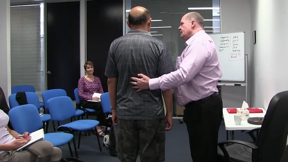 Rick Collingwood with a hand on the back of a standing student during a demonstration, while other students watch