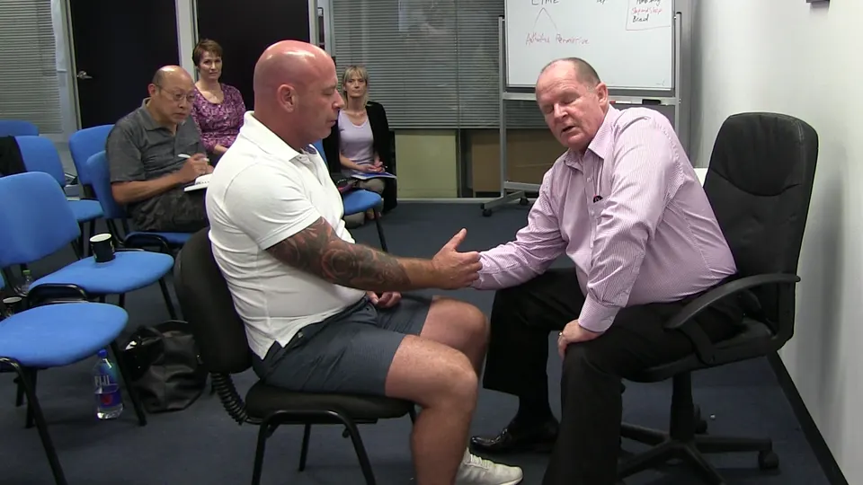 Rick Collingwood seated opposite a student, holding his forearm, while other students watch