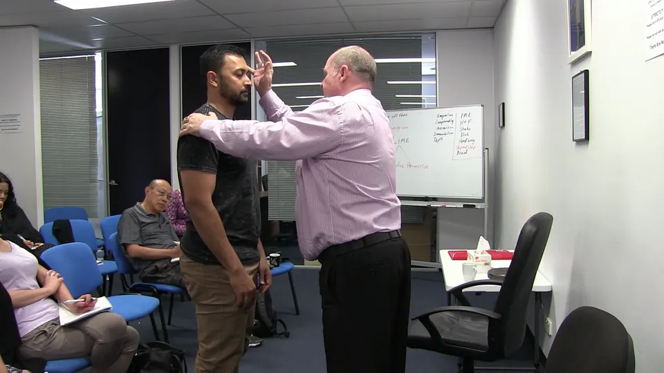 Rick Collingwood with one hand on a standing student's shoulder and the other raised near his forehead