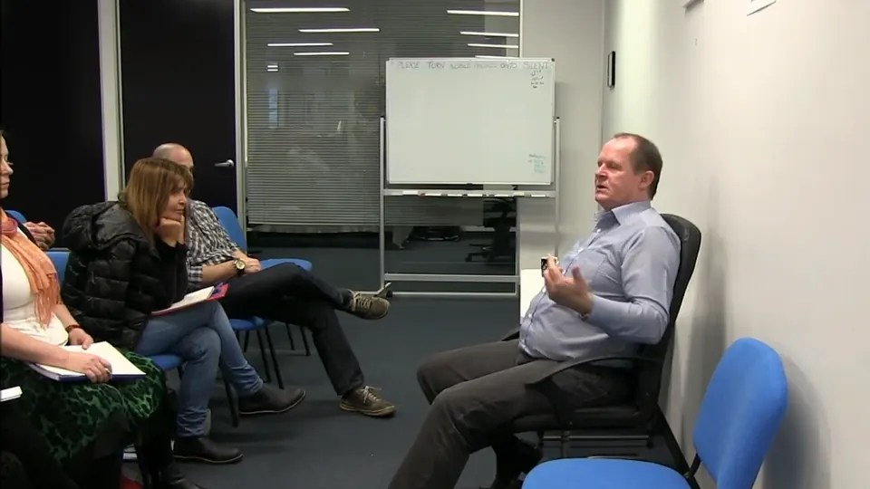 Rick Collingwood seated against the wall, talking to students with notebooks