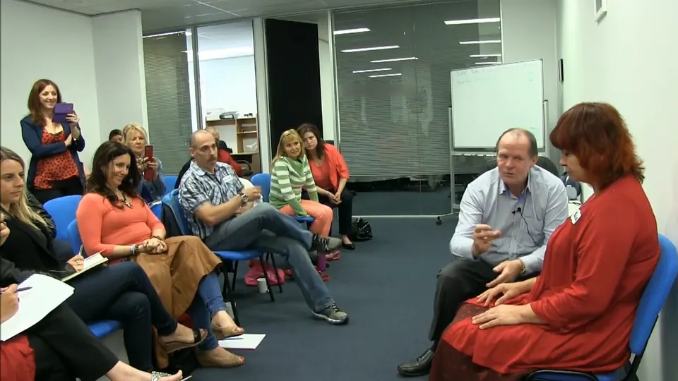 Rick Collingwood seated beside a woman in red, talking to a large group of students seated around the room