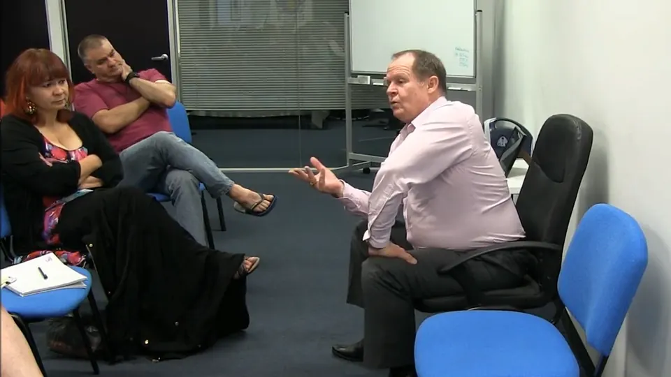 Rick Collingwood seated with a hand raised, explaining a point to two students