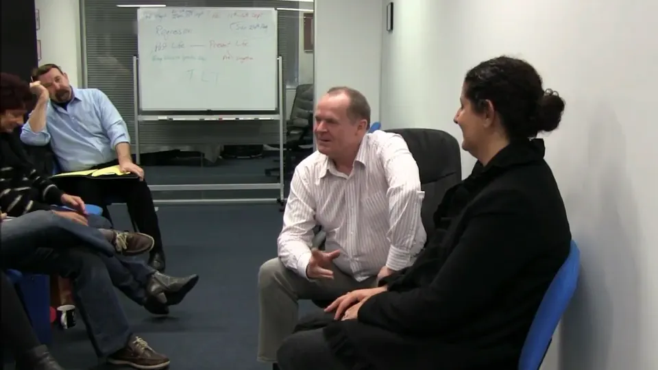 Rick Collingwood seated beside a smiling woman, gesturing as he talks, with students seated to the side